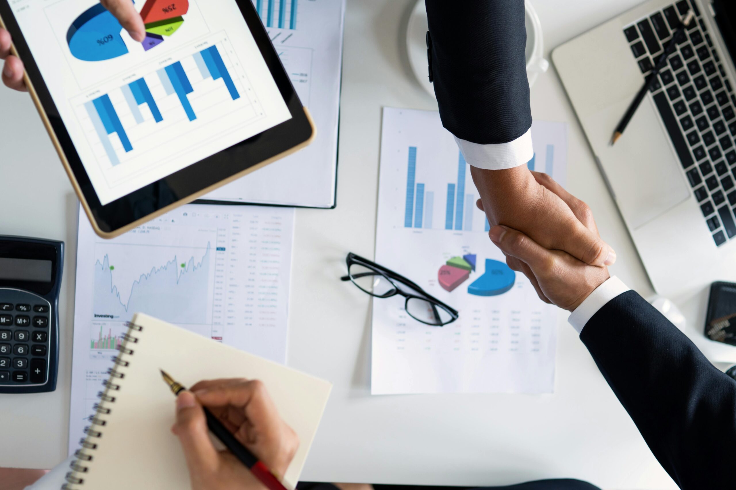 Business professionals handshake over graphs and charts in a corporate setting, symbolizing successful negotiation and agreement.